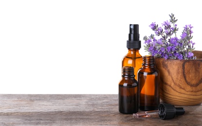 Bottles of essential oil and bowl with lavender flowers on wooden table against white background