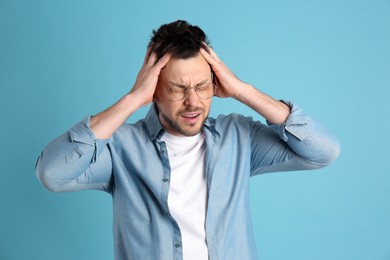 Man suffering from terrible migraine on light blue background