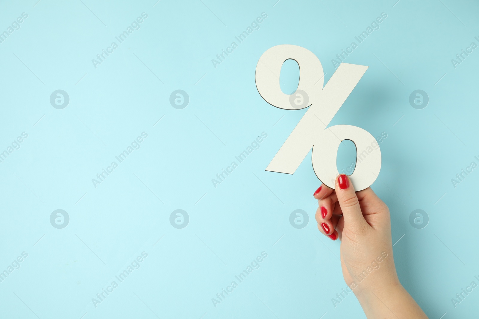 Photo of Woman holding percent sign on light blue background, closeup. Space for text