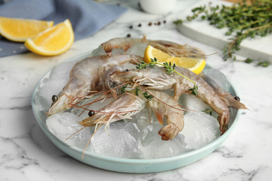 Photo of Raw shrimps with ice on marble table