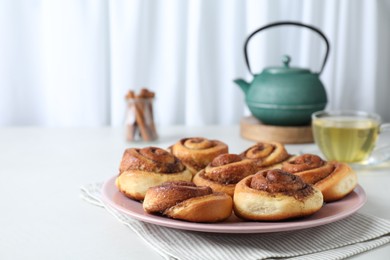 Many tasty cinnamon rolls on white table, space for text