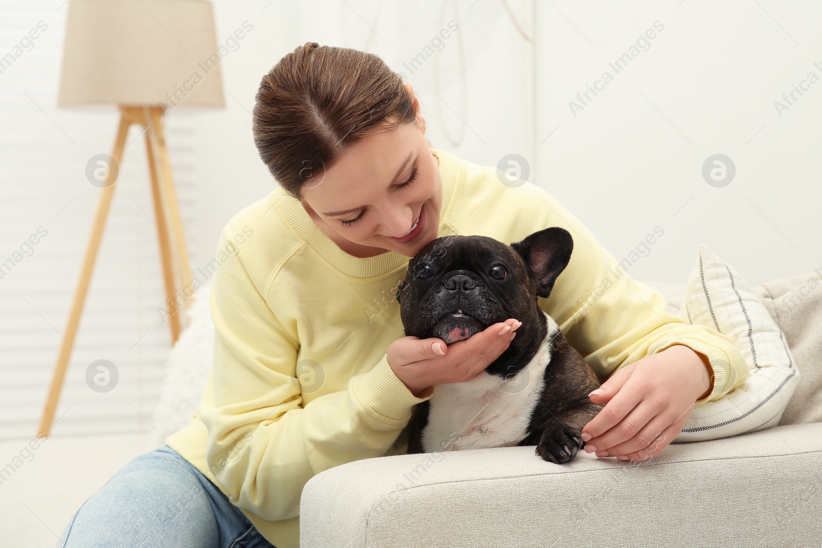 Photo of Happy woman hugging cute French Bulldog on sofa in room