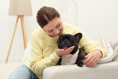 Happy woman hugging cute French Bulldog on sofa in room