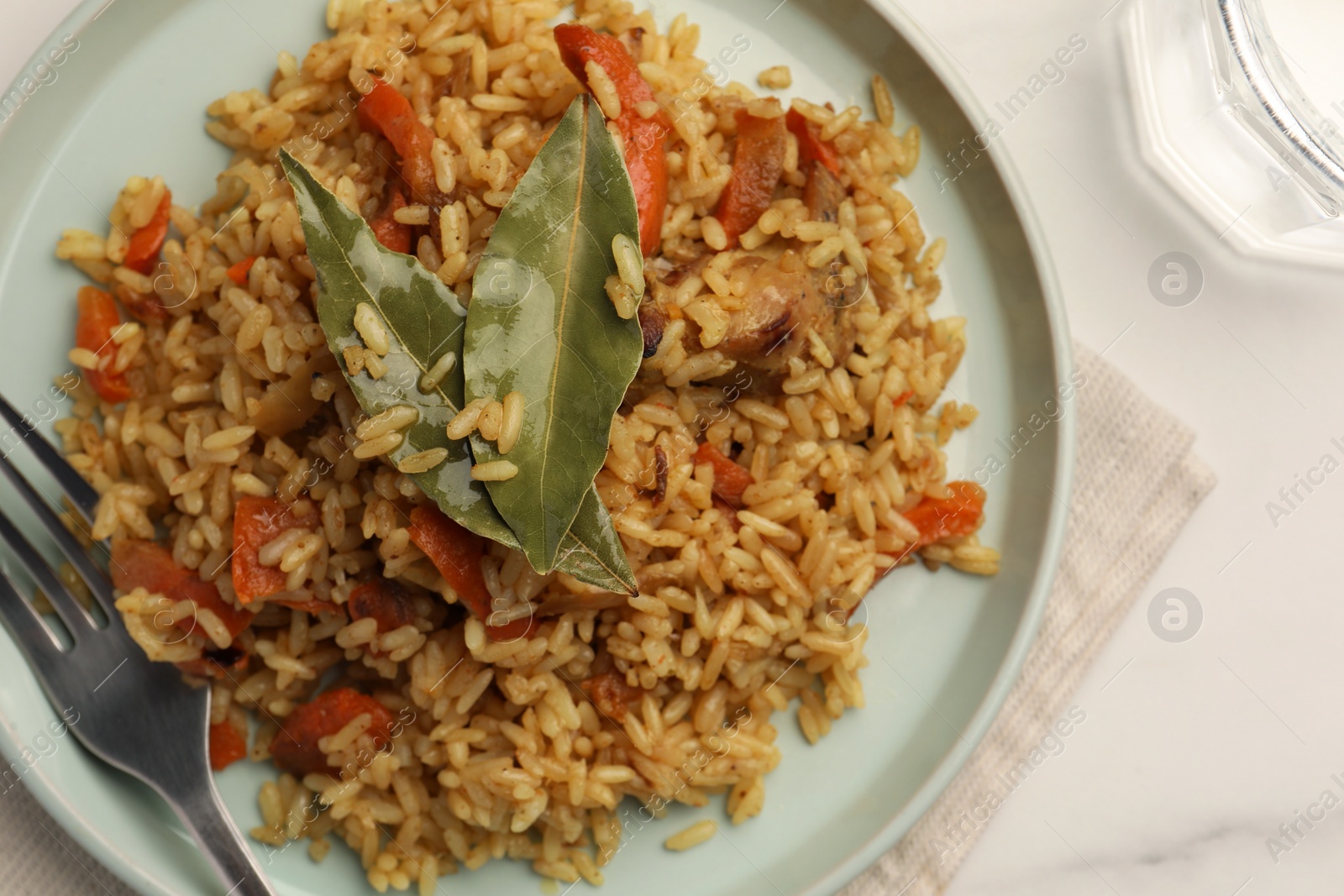 Photo of Delicious pilaf, bay leaves, fork and glass of water on white table, flat lay