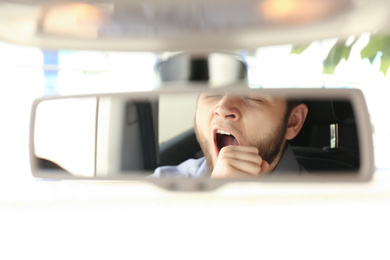 Photo of Tired man yawning while driving, reflection in rearview mirror