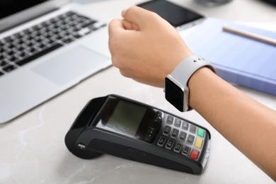 Photo of Woman using terminal for contactless payment with smart watch at table