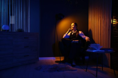 Confident young woman sitting under lamp light in cozy room at night