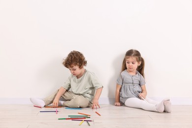 Photo of Cute little children with colorful pencils near white wall indoors