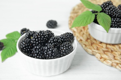 Bowls of tasty blackberries with leaves on white wooden table