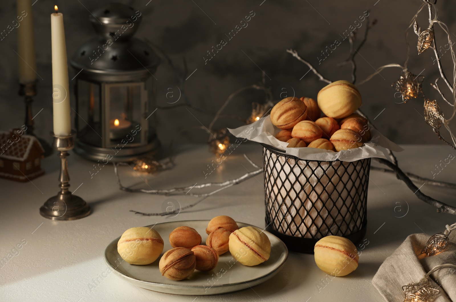Photo of Aromatic walnut shaped cookies, burning candle and decorative branch with lights on beige table. Homemade pastry carrying festive atmosphere