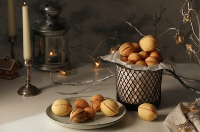 Photo of Aromatic walnut shaped cookies, burning candle and decorative branch with lights on beige table. Homemade pastry carrying festive atmosphere