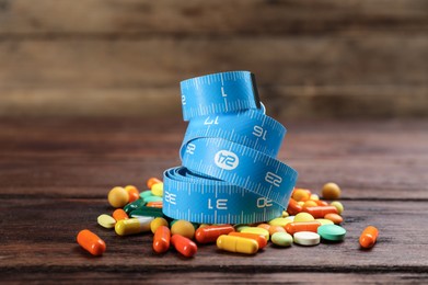 Photo of Different weight loss pills and measuring tape on wooden table