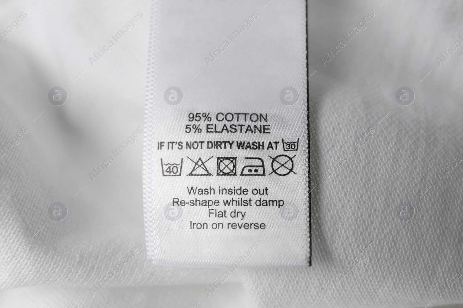 Photo of Clothing label with care symbols and material content on white shirt, closeup view