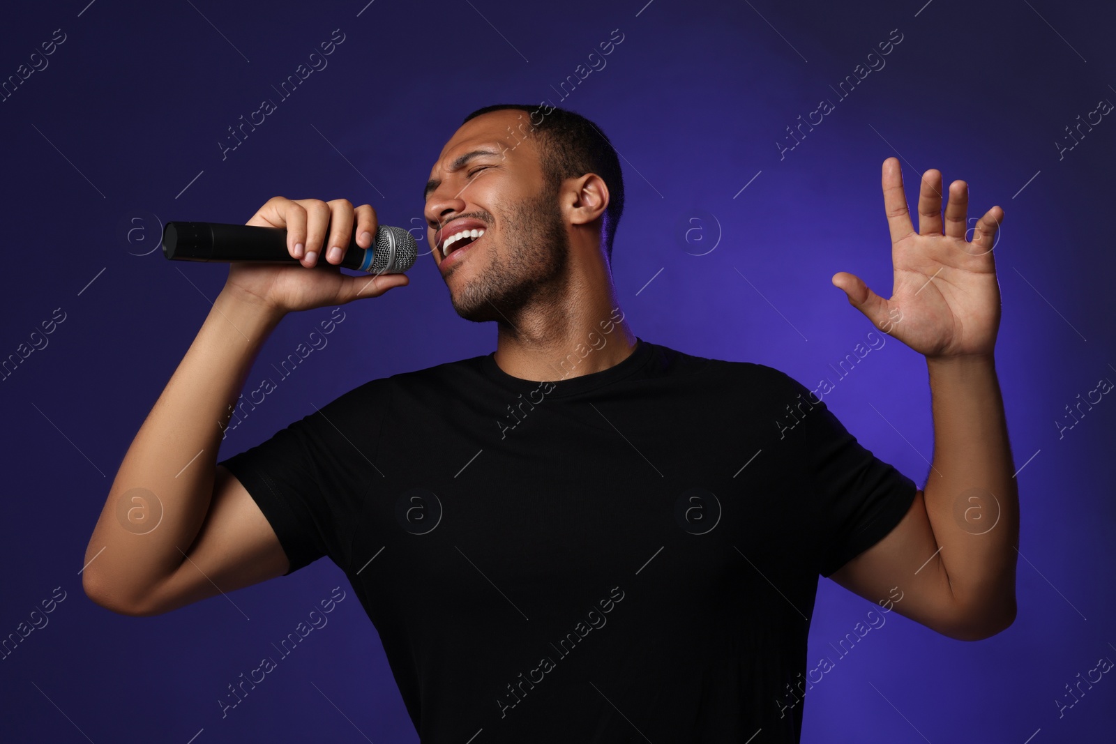 Photo of Handsome man with microphone singing on blue background
