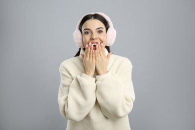 Photo of Beautiful young woman wearing earmuffs on light grey background