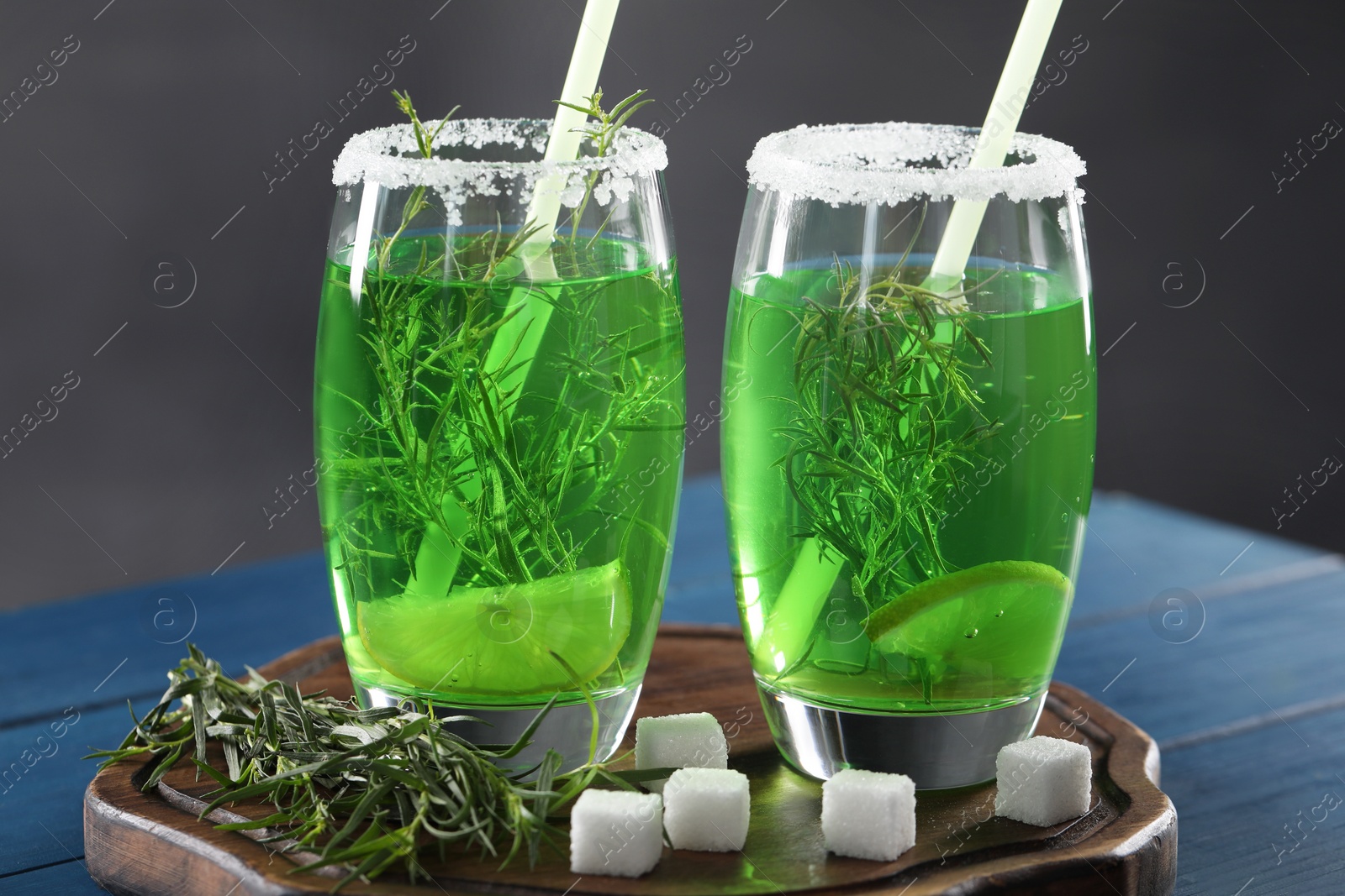 Photo of Glasses of homemade refreshing tarragon drink, sprigs and sugar cubes on blue wooden table, closeup