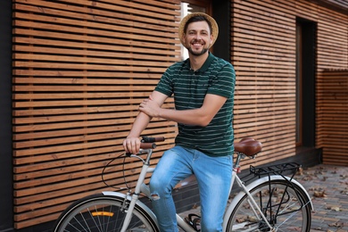 Man with bicycle on street near wooden wall