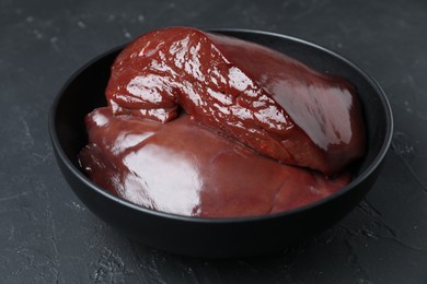 Photo of Pieces of raw beef liver in bowl on black table, closeup