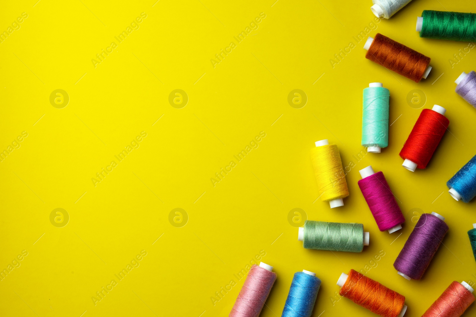 Photo of Different colorful sewing threads on yellow background, flat lay. Space for text