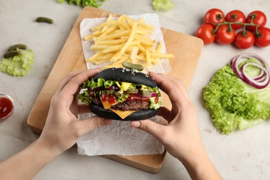 Photo of Woman holding black burger at served table, closeup