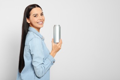 Beautiful happy woman holding beverage can on light grey background. Space for text