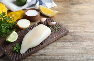 Photo of Fresh raw squid tube with lime, parsley and garlic on wooden table, space for text