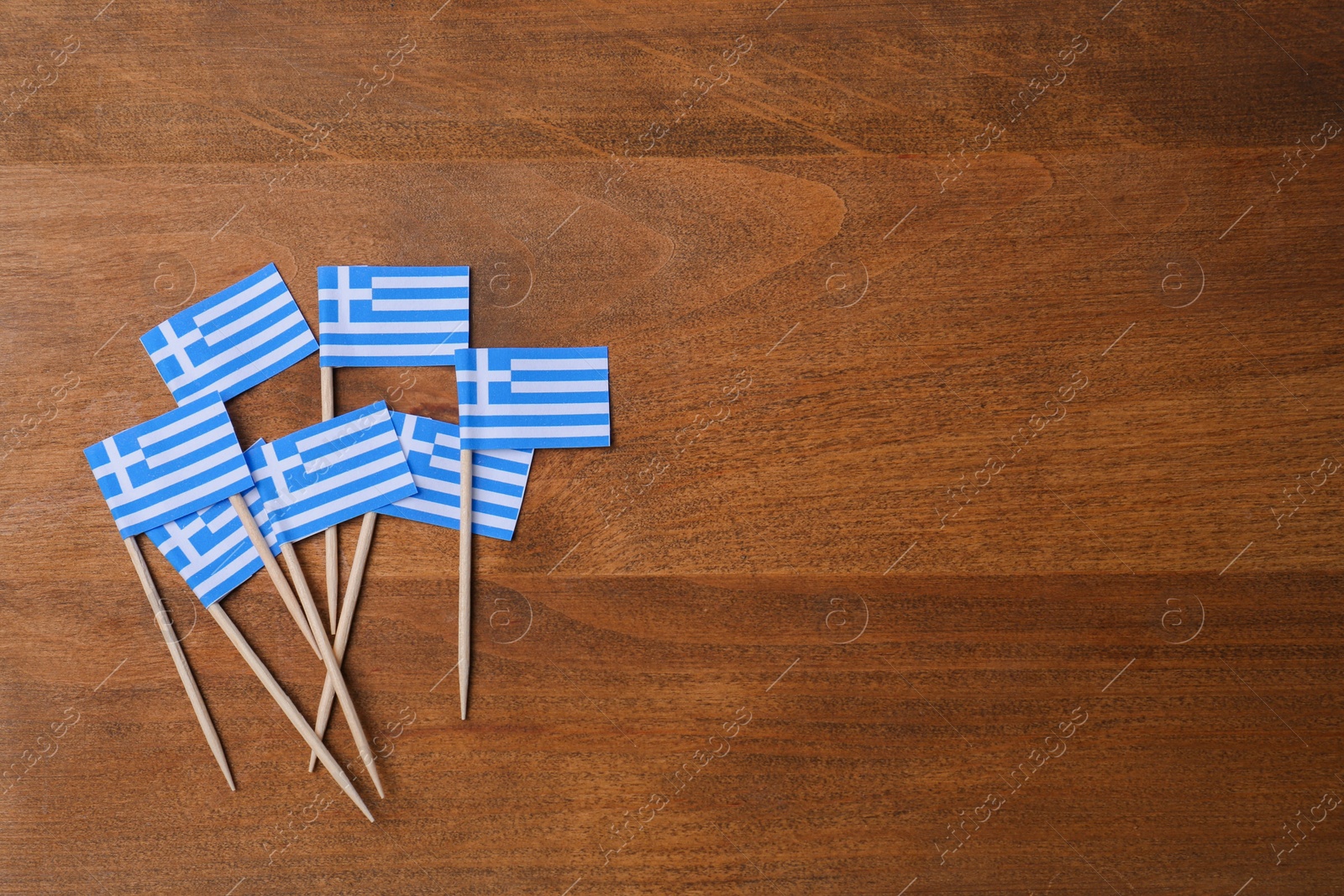Photo of Small paper flags of Greece on wooden table, flat lay. Space for text
