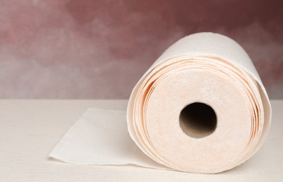 Photo of Roll of paper towels on white wooden table near pink wall, closeup. Space for text