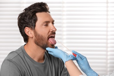Photo of Doctor taking throat swab sample from man`s oral cavity indoors. Space for text