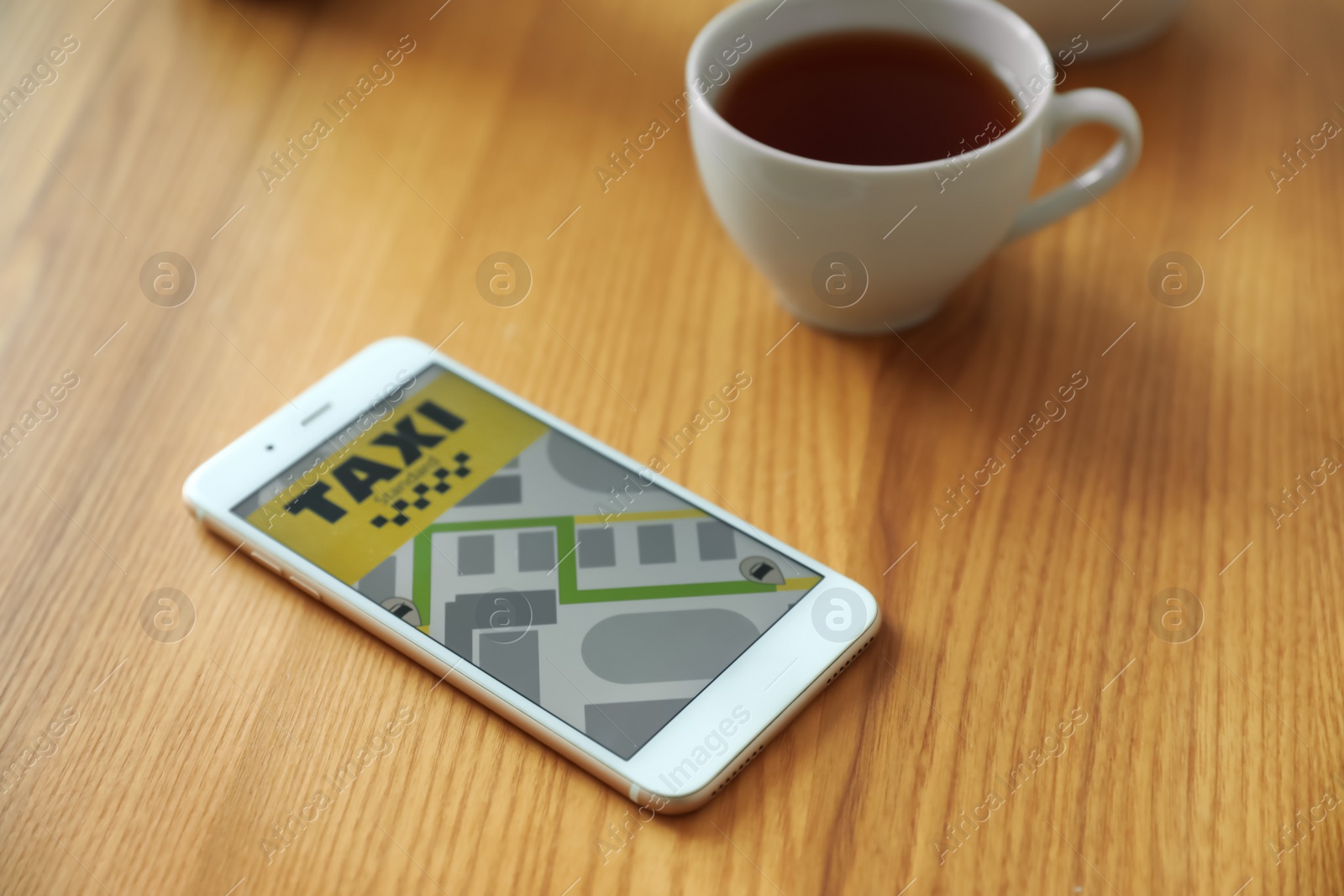 Photo of Smartphone with taxi application and cup of tea on wooden table