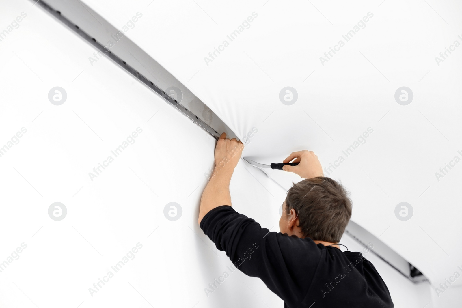 Photo of Repairman installing white stretch ceiling in room