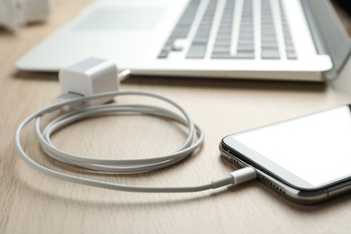 Photo of Smartphone and USB charger on wooden table, closeup. Modern technology