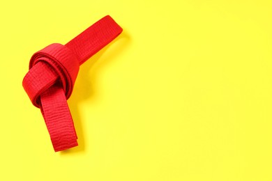 Red karate belt on yellow background, top view. Space for text