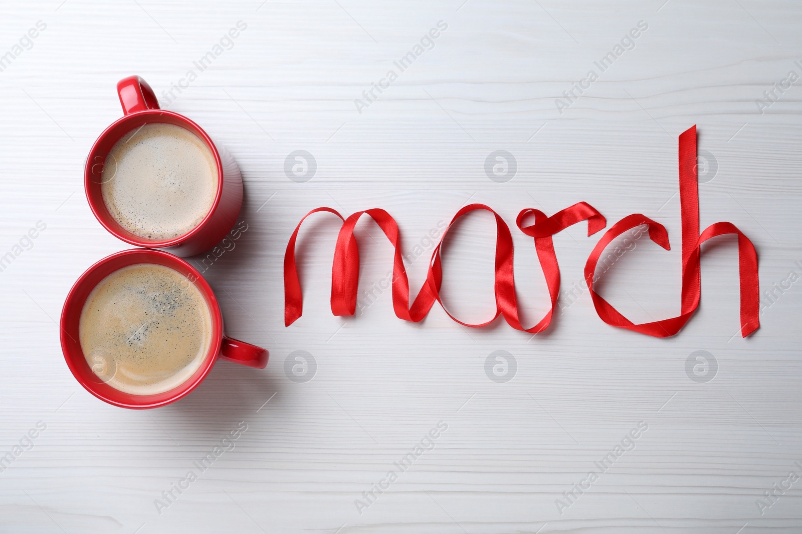 Photo of 8 March greeting card design with cups of coffee and red ribbon on white wooden background, flat lay. International Women's day