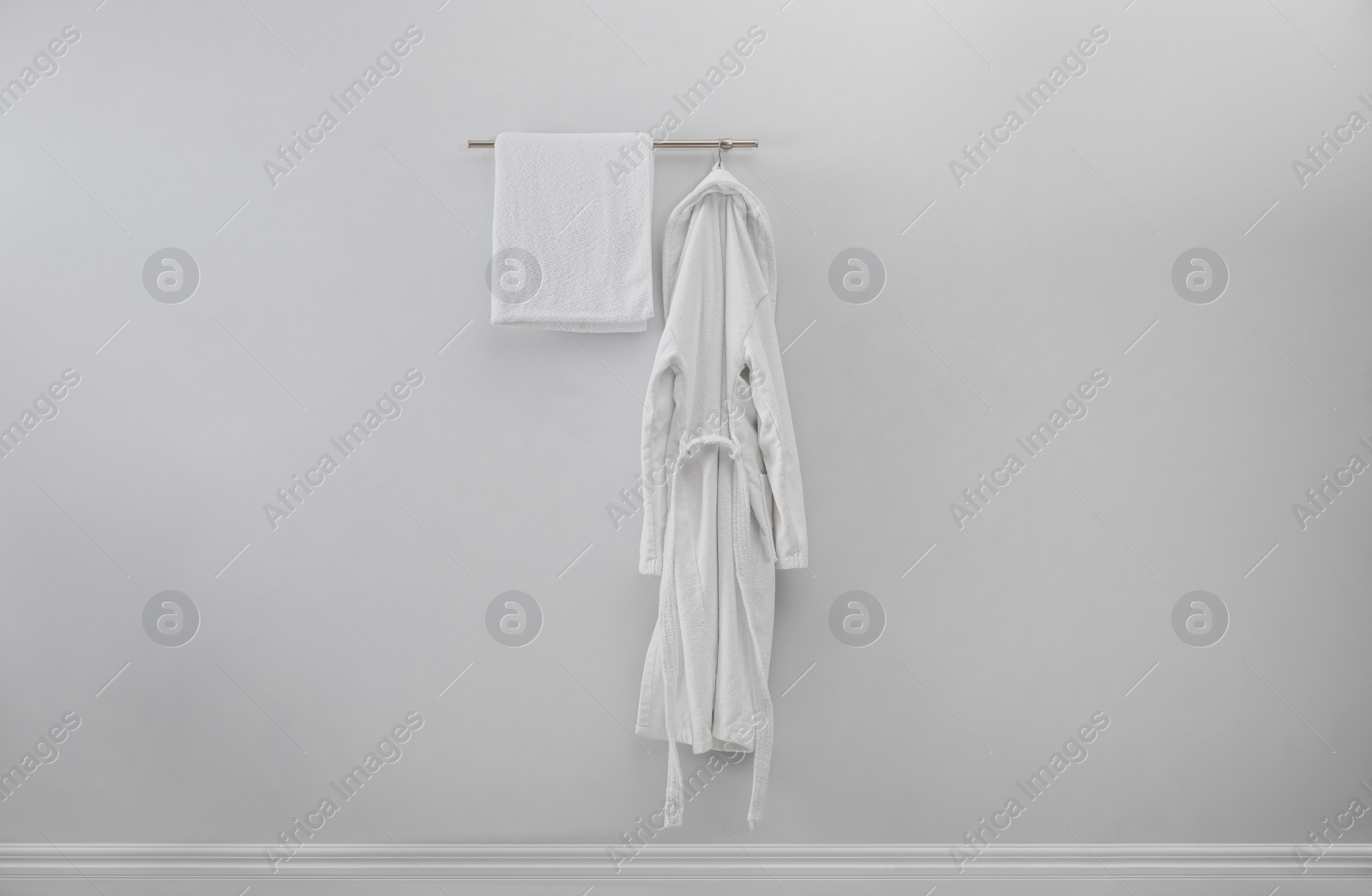 Photo of Rack with clean bathrobe and towel on light wall