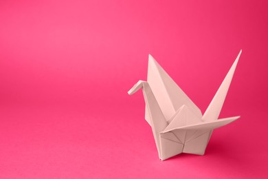 Photo of Origami art. Handmade paper crane on pink background, space for text