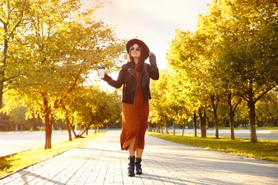 Photo of Beautiful young woman with cup of coffee wearing stylish clothes in autumn park