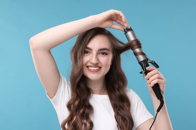Photo of Beautiful young woman using curling hair iron on light blue background