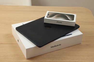Photo of Leiden, Netherlands - October 6, 2023: Modern black MacBook Air and box from iPhone 15 Pro Max on wooden table