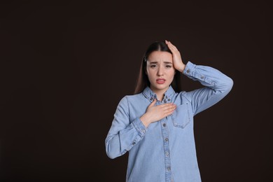 Young woman suffering from cold on dark background, space for text