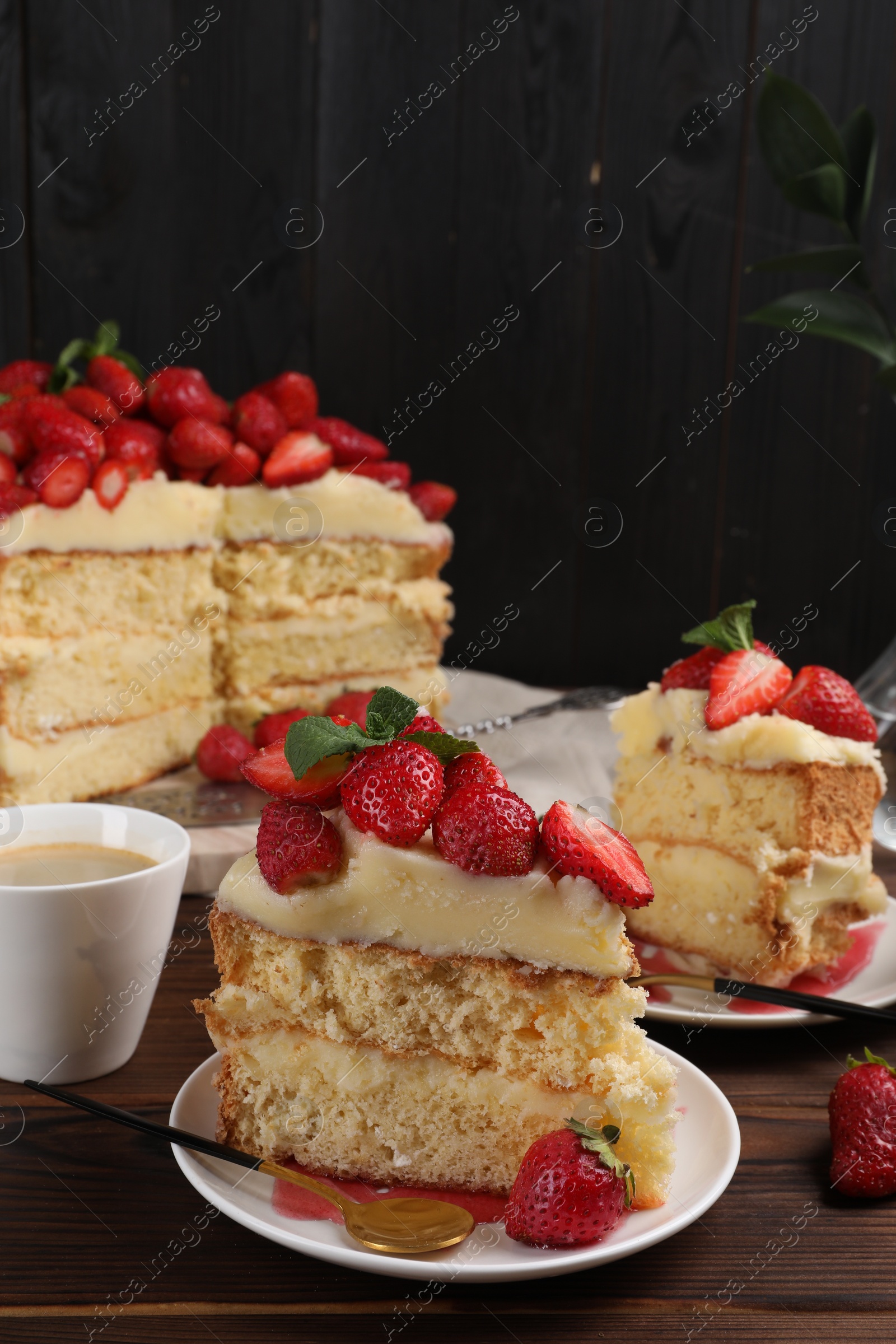 Photo of Tasty cake with fresh strawberries, mint and cup of drink on wooden table