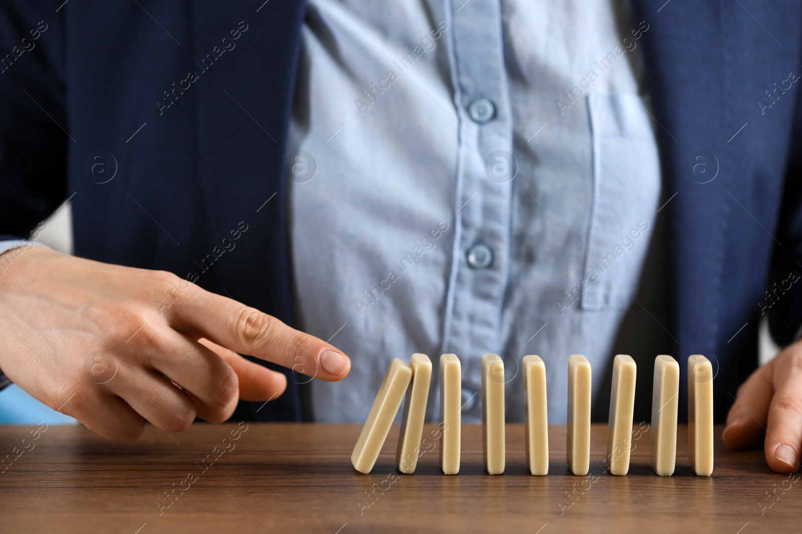 Photo of Woman causing chain reaction by pushing domino tile at table, closeup