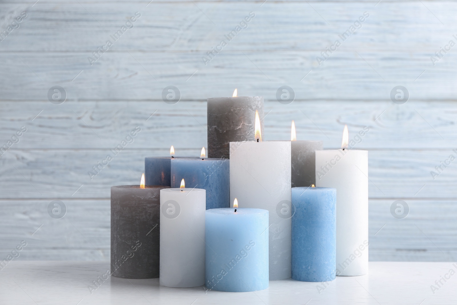 Photo of Set of burning candles on table against light wooden background