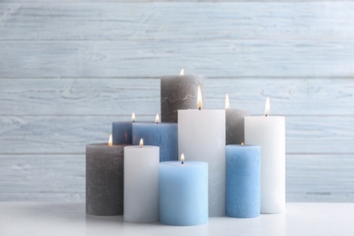 Photo of Set of burning candles on table against light wooden background