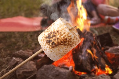 Image of Delicious puffy marshmallow roasting over bonfire outdoors