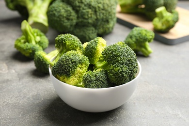 Photo of White bowl of fresh green broccoli on grey stone table, closeup view