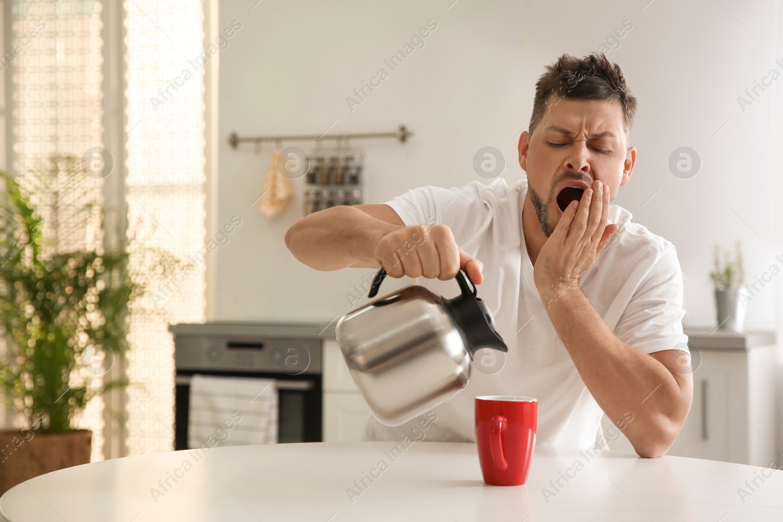 Photo of Sleepy man pouring coffee into cup at home in morning