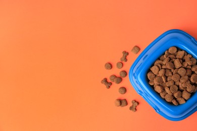 Dry pet food in feeding bowl on orange background, flat lay. Space for text