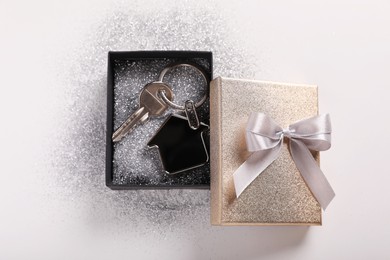 Photo of Key with trinket in shape of house, glitter and gift box on light grey background, flat lay. Housewarming party