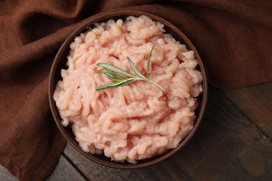 Fresh raw minced meat and rosemary in bowl on wooden table, top view